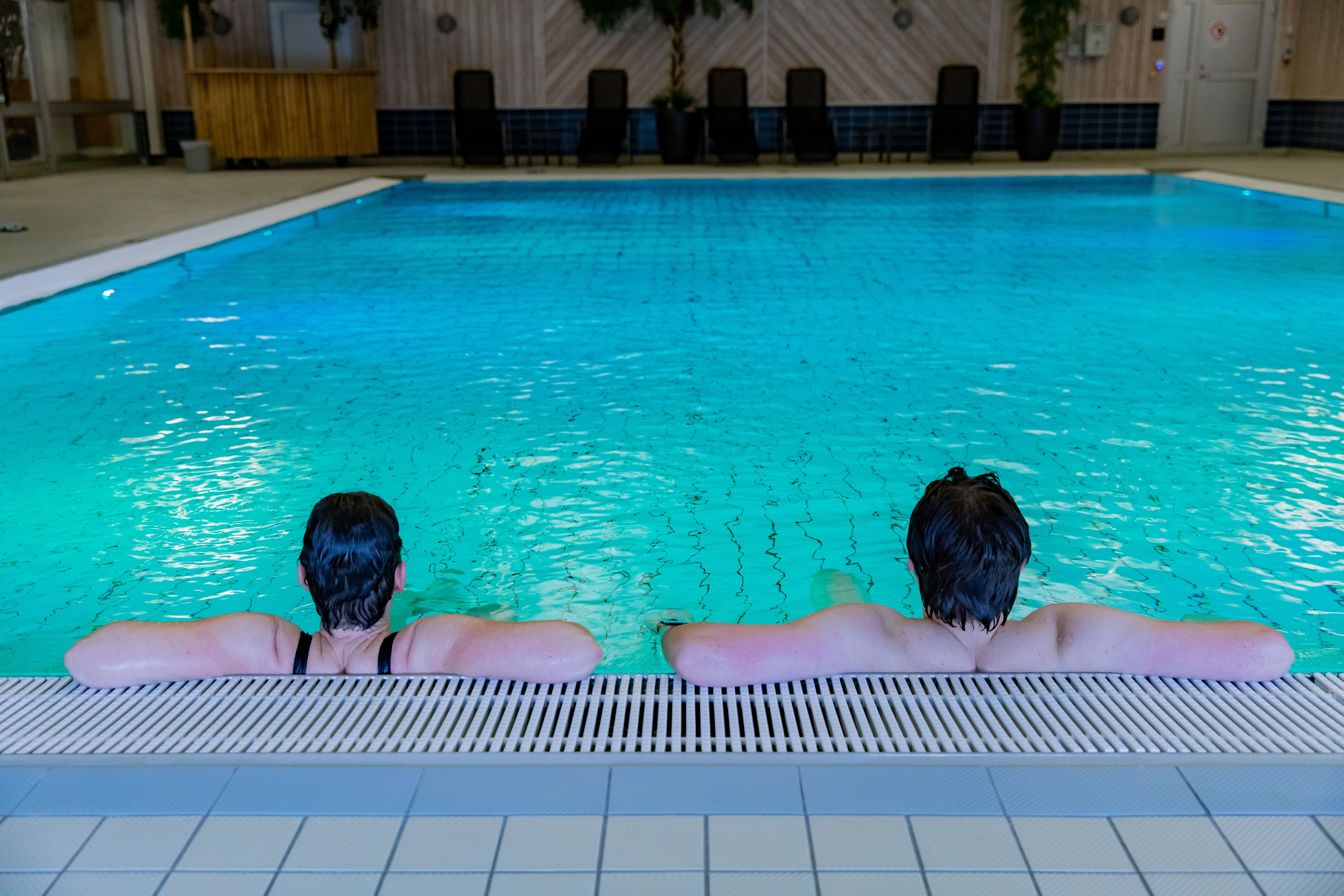 Två personer vilar med armarna på bassängkanten i en turkos bassäng.